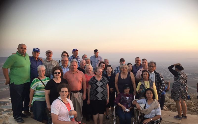 A Christian group tour gathered at a summit viewpoint overlooking the hills of Israel at sunset